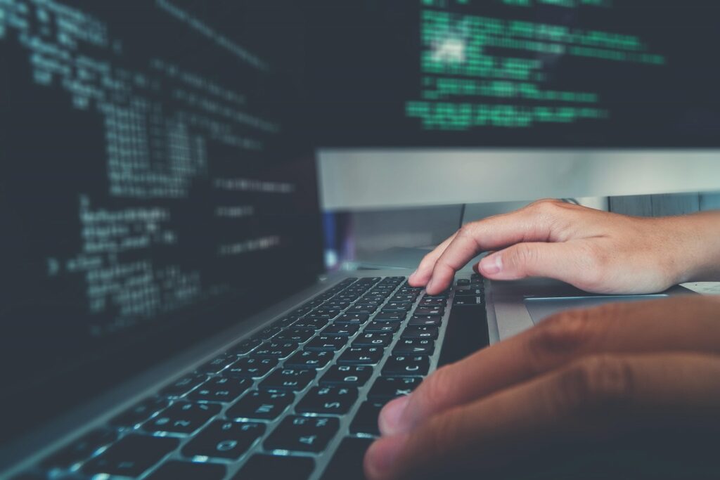 Developer typing on a mac book with code in the background.