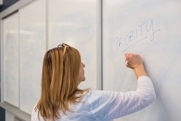 Woman writing on a white board trying to capture the priorities of her team.