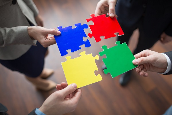 4 employees collaborating to put 4 different colour puzzle pieces together.