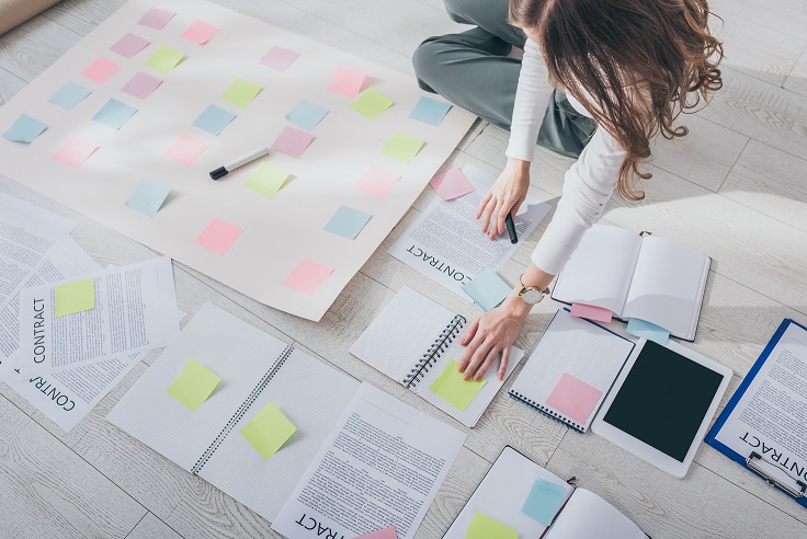 Young woman looking at all of her notes and post it notes on the ground
